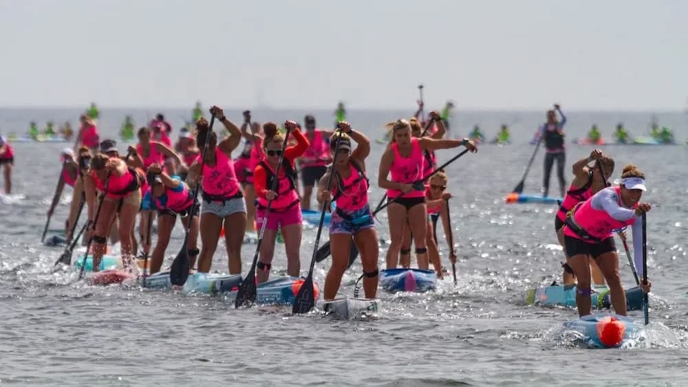 Race pack of paddlers in matching jerseys leaving the start line